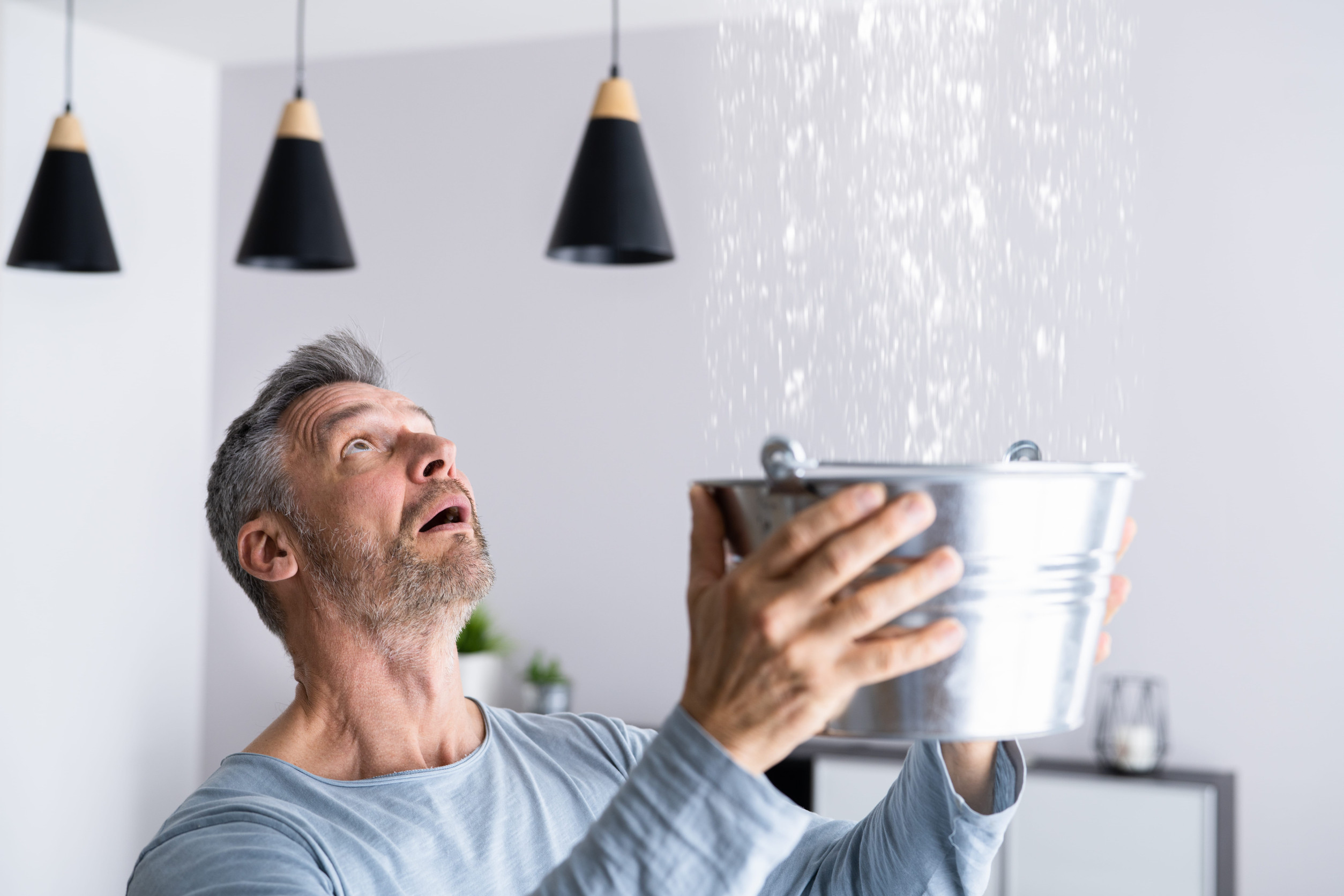 Man holding bucket to catch leaking water